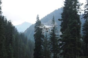 a white drone flying in the misty forrest