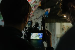 a picture taken from behind of a man who is filming a video of a climber in a climbing hall