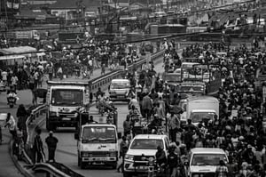 a wide street with a couple of cars and a lot of people all over the place in black and white
