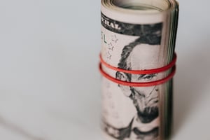 a close up of a roll of 5 dollar bills featuring Abraham Lincoln held together by a red rubber band