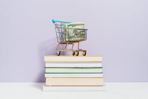 a mini shopping cart carrying paper money on a stack of books